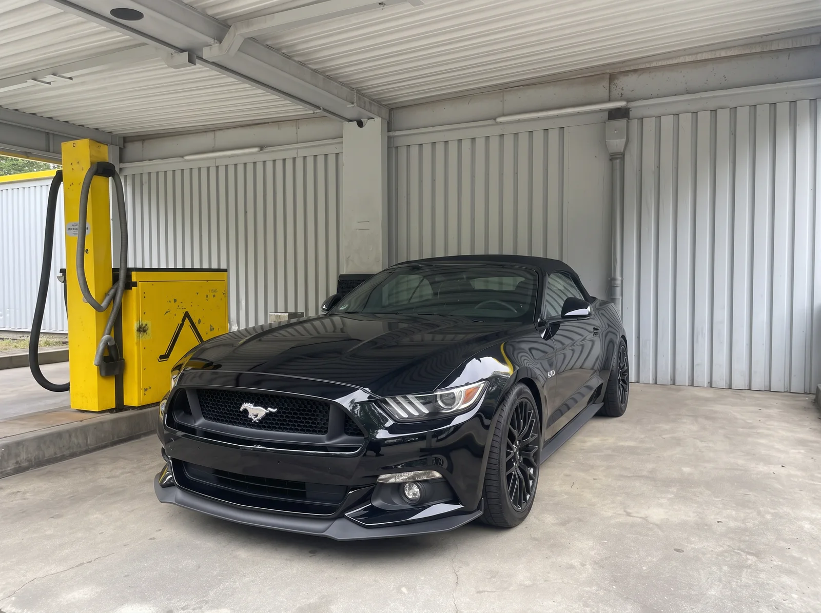 Schwarzes Ford Mustang Cabriolet mit geschlossenem Verdeck unter einem Waschplatzdach