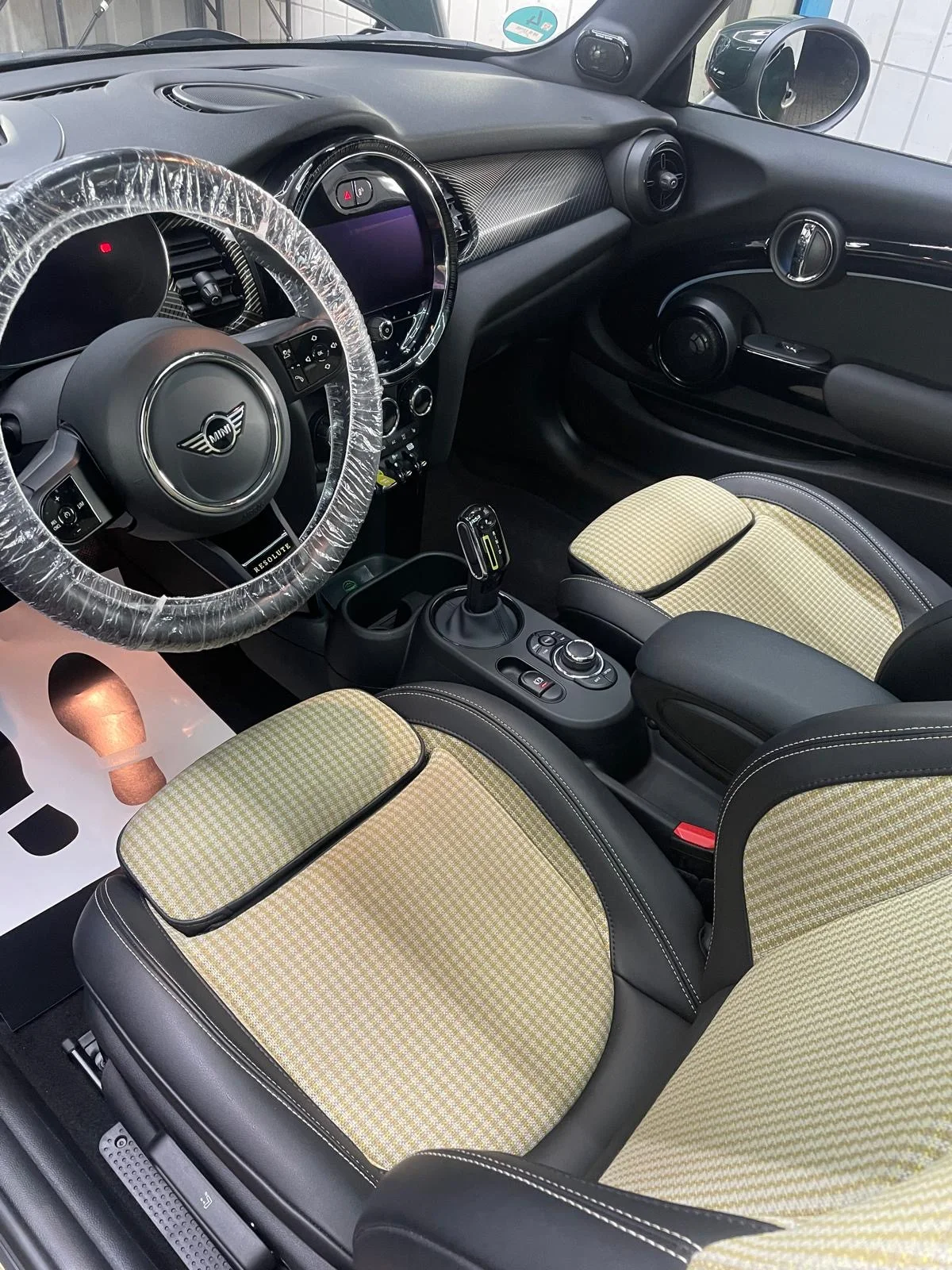 MINI-Innenraum mit hell gemusterten Sitzflächen, rundem Zentraldisplay und Lenkradschutz